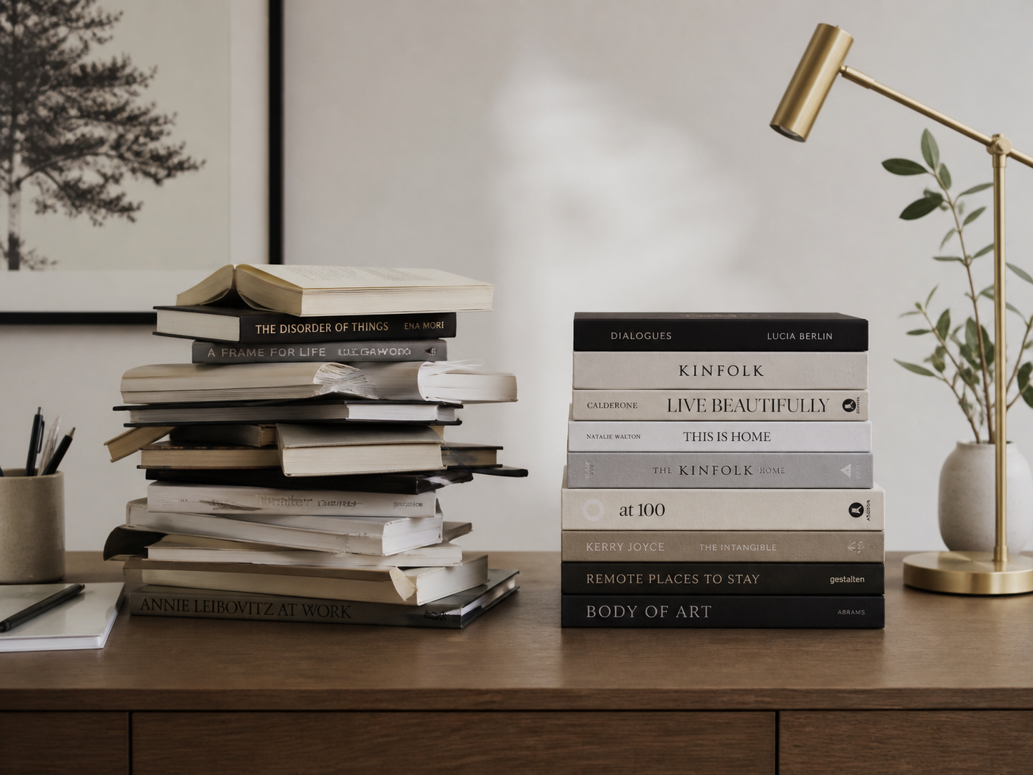 A stack of research books on a writing desk beside a brass lamp
